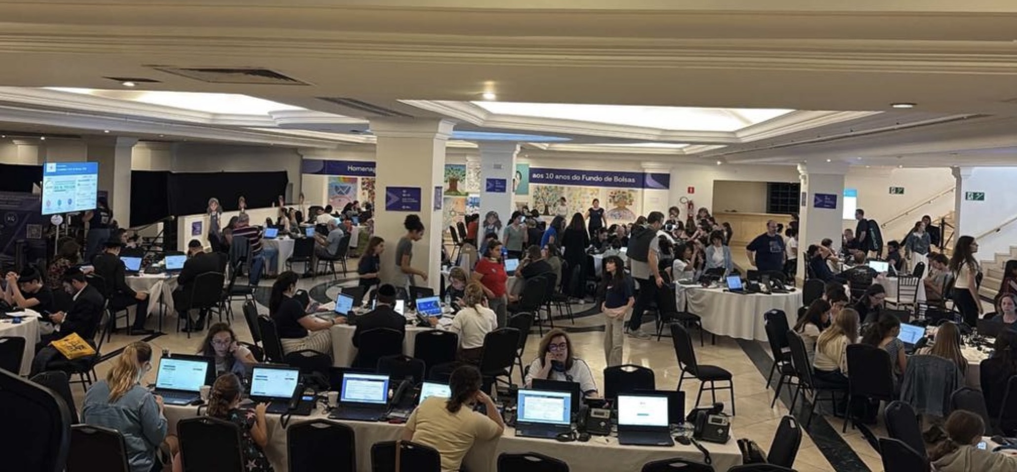 Sala de voluntarios trabajando en la campaña del Fondo de Becas, con mesas llenas de laptops y teléfonos
